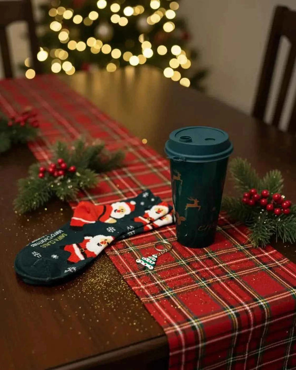 Green travel cup with Santa socks and a tree keyring on a tartan table runner