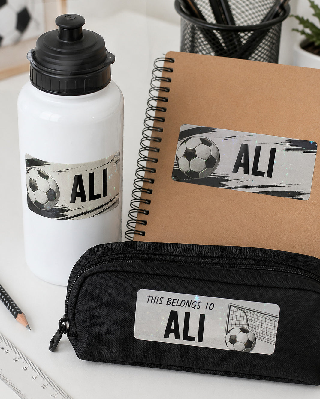 Holographic football name labels on a white sports bottle, notebook and pencil case