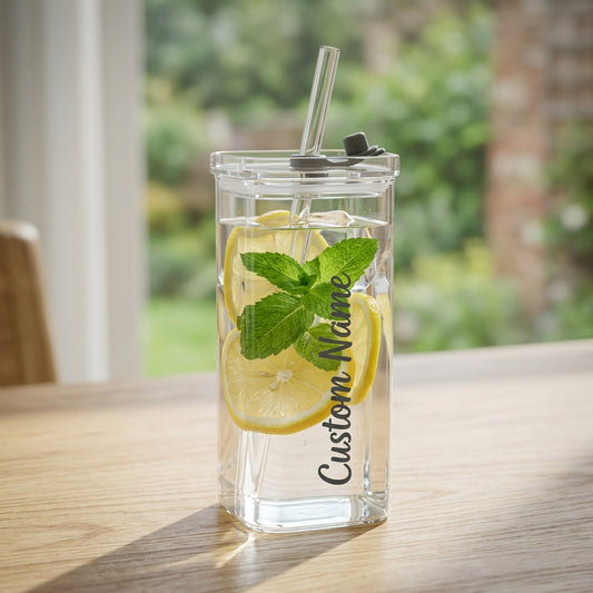 Clear tumbler with lemon slices, mint leaves, and a straw on a wooden surface with a blurred green outdoor background.