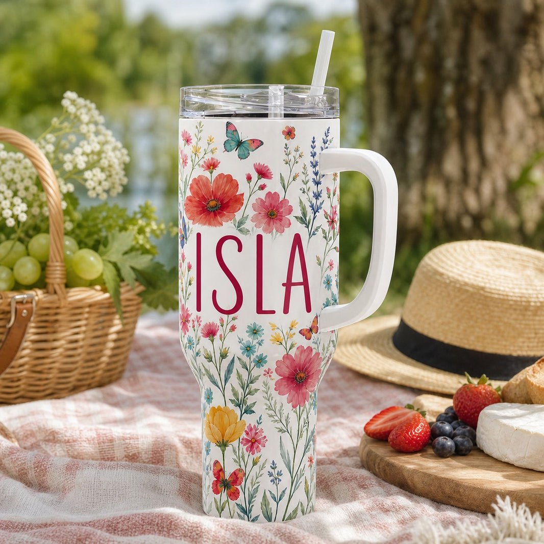 Personalised 40oz stainless steel tumbler with wildflower design and the name Isla at a summer picnic
