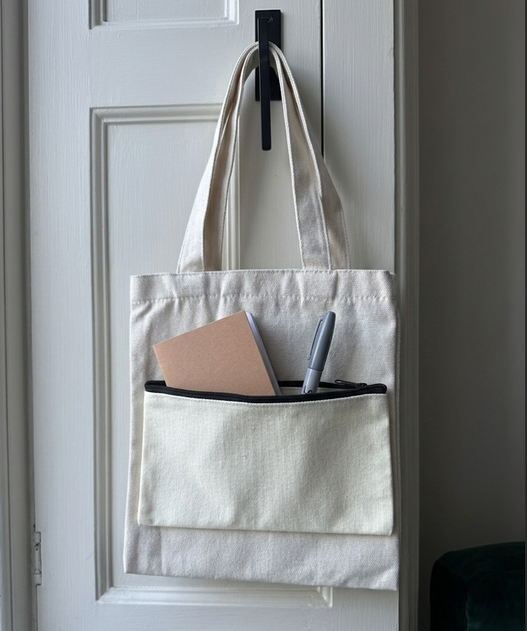 White tote bag with a pocket containing a notebook and pen, hanging on a door handle.