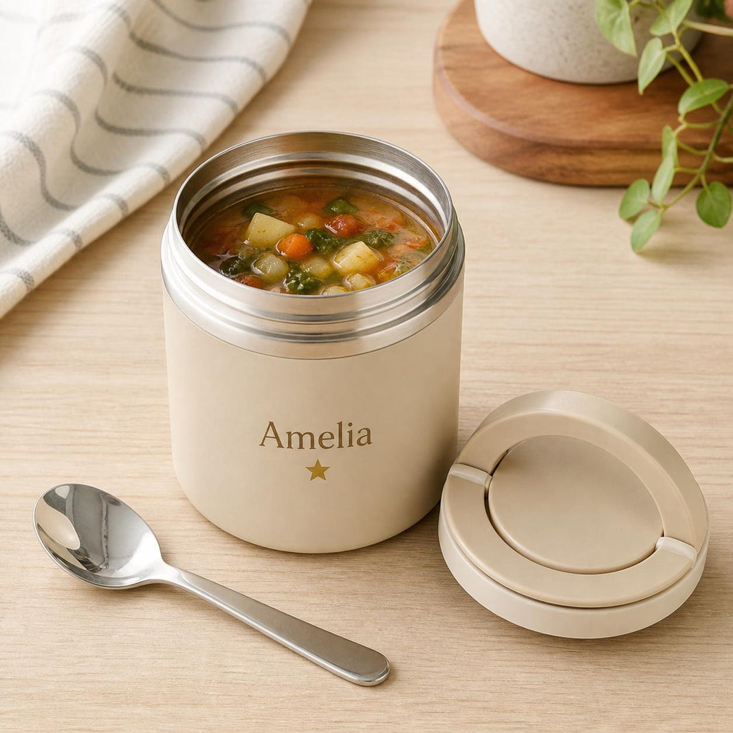 Cream food jar printed Amelia with a star, open and filled with vegetable soup beside a spoon