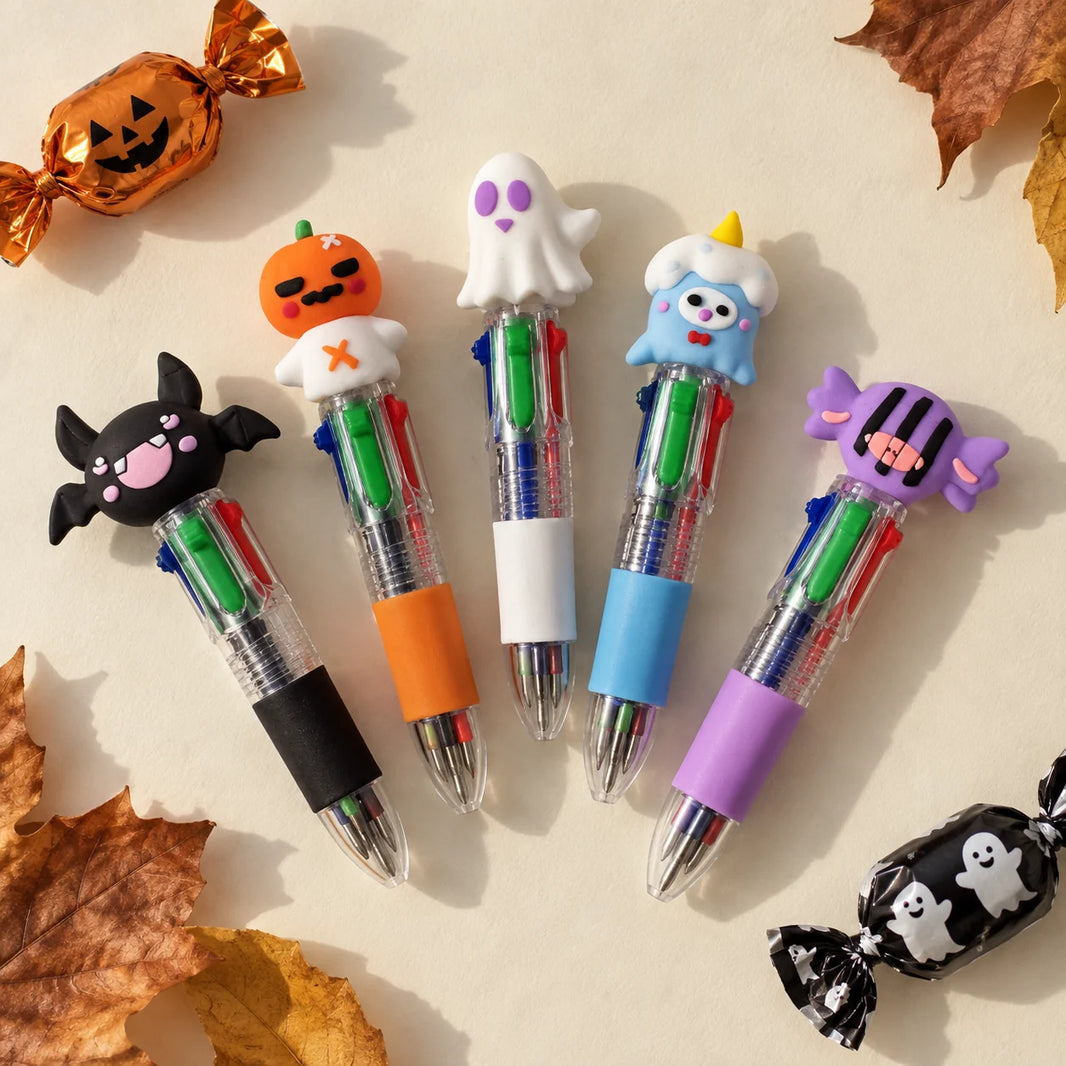 Flat lay of five Halloween four-colour ballpoint pens with bat, pumpkin, ghost, monster and sweet toppers on a cream background