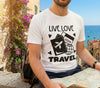 Person wearing a white t-shirt with 'Live Love Travel' design, sitting by a scenic coastal town.