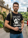 Man wearing a 'Live Love Travel' t-shirt with a camera, standing in a scenic village setting.