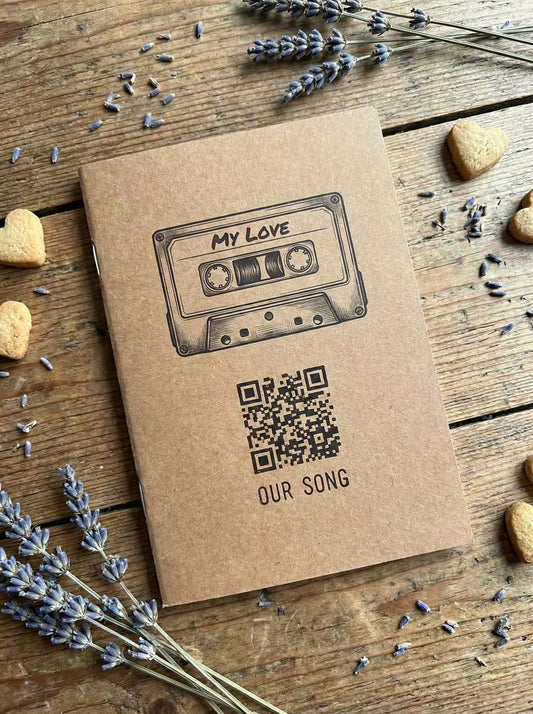 Kraft paper notebook with cassette tape and QR code design on a wooden surface with lavender flowers.