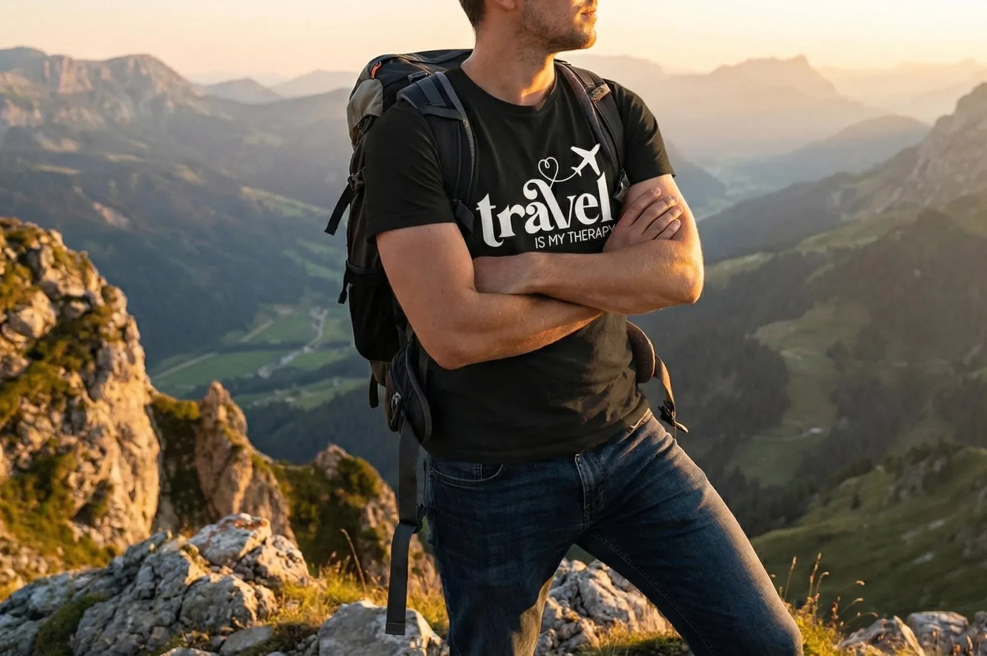 Person with a backpack and 'Travel is my Therapy' t-shirt standing on a mountain with a scenic view.