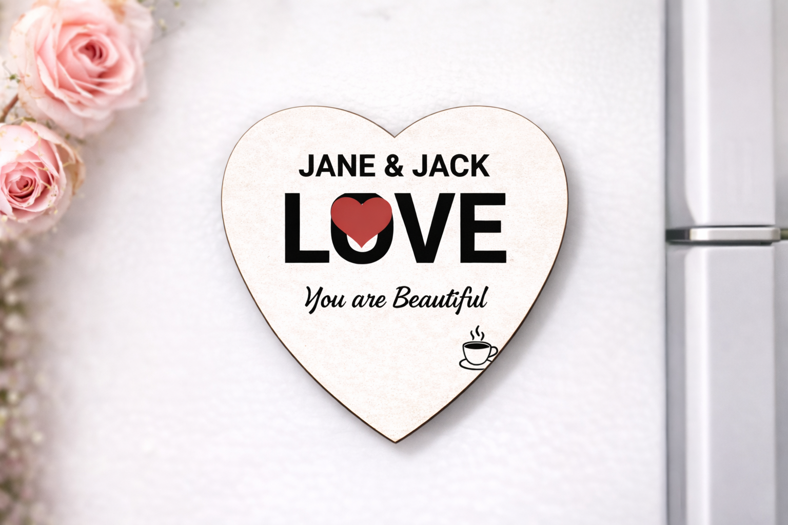 Heart-shaped wooden plaque with 'JANE & JACK LOVE You are Beautiful' text on a white surface with pink roses.